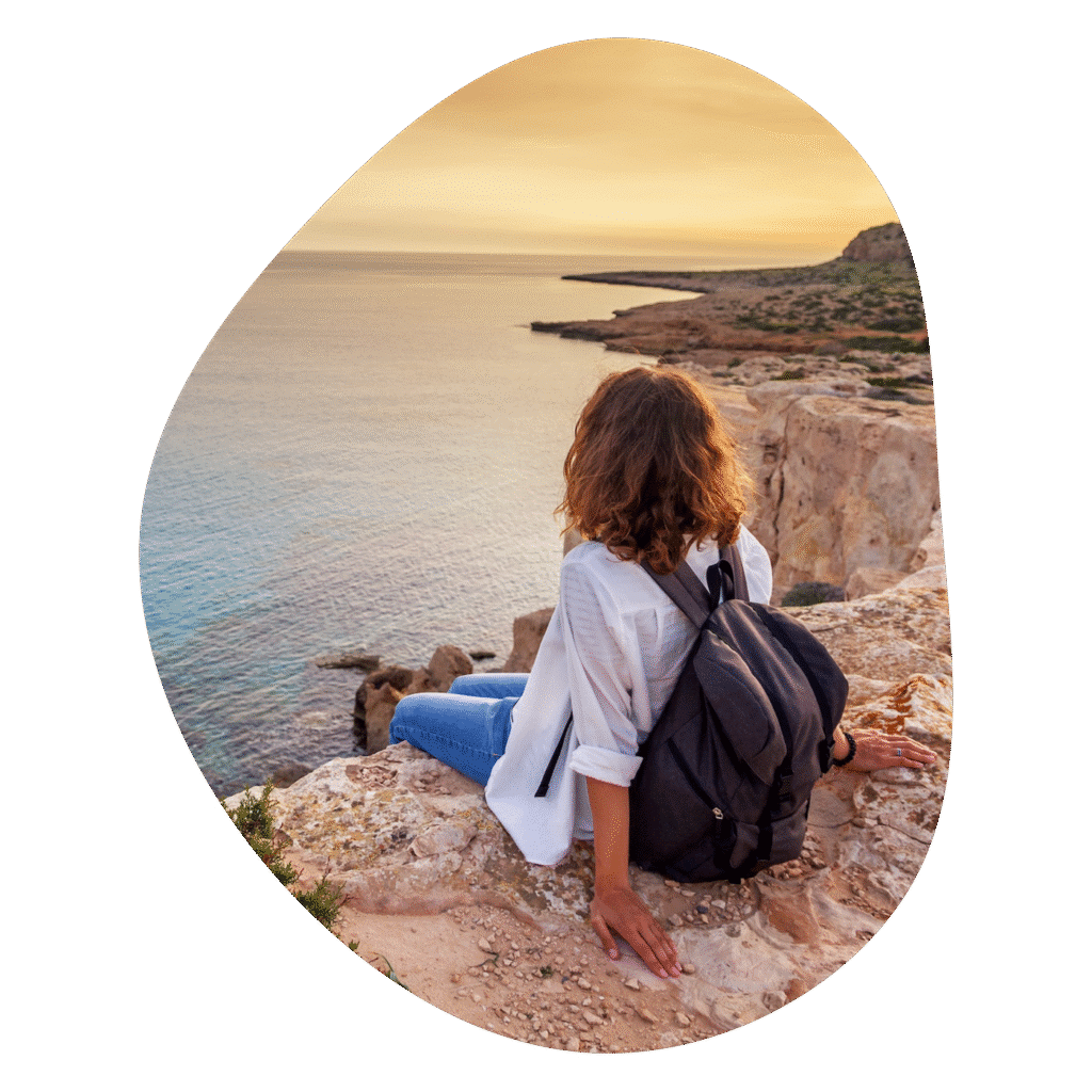 Girl sitting on cliff, looking at the sunset